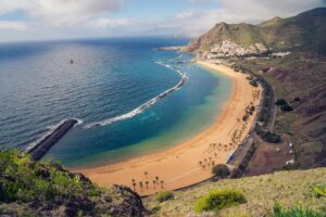 Playa de Tenerife con arena volcánica y aguas cristalinas, ideal para disfrutar del sol y el mar durante todo el año.