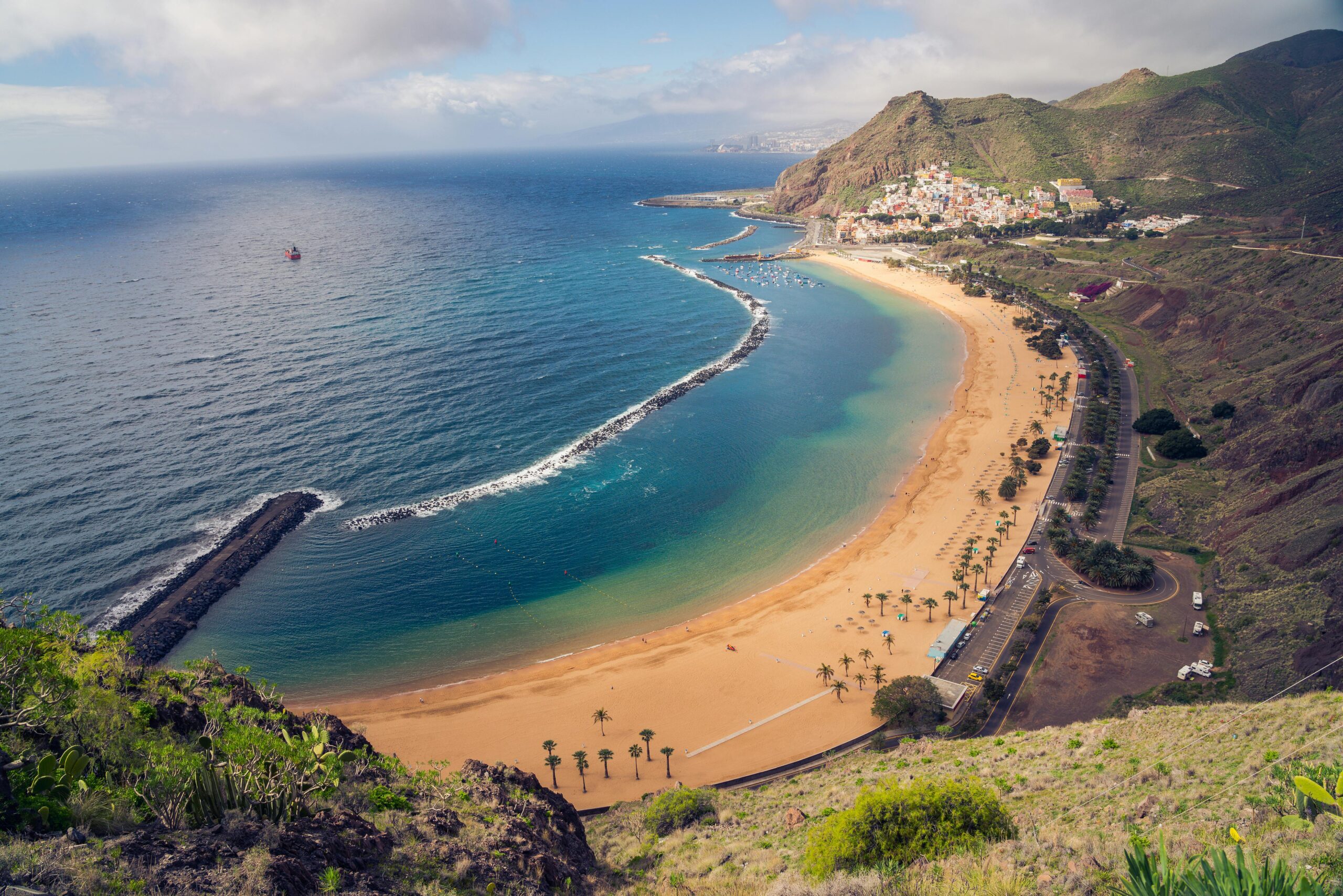 Playa de Tenerife con arena volcánica y aguas cristalinas, ideal para disfrutar del sol y el mar durante todo el año.
